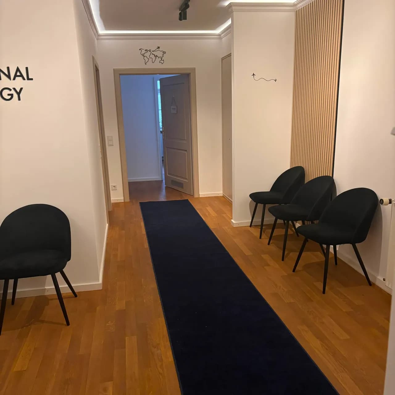 Flur des Wartebereichs mit schwarzen Stühlen, einem dunkelblauen Läufer und einer Holzlamellenwand